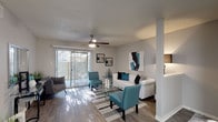 Located at 2502 Babcock Rd in San Antonio, Texas, this single-floor residence offers a thoughtfully designed layout with a cohesive teal and gray color palette throughout. The living room serves as the centerpiece of the home, featuring wood-style flooring, a ceiling fan with integrated lighting, and a sliding glass door framed by vertical blinds that invites abundant natural light and provides access to an outdoor area. The open layout extends to a dedicated dining space, creating a seamless flow for everyday living and entertaining. The kitchen is equipped with gray cabinetry, a subway tile backsplash, light quartz-style countertops, and black appliances, including an electric range with an overhead exhaust hood. A secondary living or flex room offers carpeted flooring, a ceiling fan, and a large window dressed with bold patterned curtains, providing a versatile space for relaxation or use as an additional bedroom. The bedroom features carpeted flooring, a ceiling fan, a natural-light window with blinds, and ample room for furnishings. The bathroom is finished with a granite-style countertop vanity and a tiled shower-tub combination. Throughout the residence, neutral wall tones and consistent design accents create a warm and inviting ambiance.