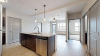This 2-bedroom, 2-bathroom residence is thoughtfully designed with a practical, single-floor layout that maximizes both comfort and functionality. The open-concept kitchen and living area serves as the heart of the home, anchored by a large center island with a granite countertop, undermount sink, and pendant lighting overhead. Rich dark cabinetry pairs with stainless steel appliances — including a refrigerator, range, and dishwasher — to create a polished, contemporary kitchen. Light wood-style flooring runs throughout the main living areas, enhancing the bright and airy atmosphere. The living room benefits from large windows and direct access to a private balcony, offering outdoor views and abundant natural light. Both bedrooms feature plush carpeting and well-sized windows. The primary bedroom includes a spacious walk-in closet outfitted with wire shelving. The bathrooms are finished with granite-topped vanities and dark cabinetry consistent with the kitchen's aesthetic. A dedicated laundry room provides added convenience and houses the water heater and HVAC systems. Clean neutral tones and modern fixtures throughout lend the space a cohesive, move-in-ready appeal.