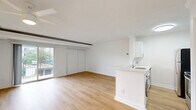 Located at 100 S Van Dorn St, Unit 303, in Alexandria, Virginia, this efficiently designed single-floor unit offers a clean, modern aesthetic throughout. The open-concept kitchen and living area serves as the heart of the space, finished with warm light wood flooring and crisp white walls that create a bright, airy atmosphere. The kitchen features white cabinetry, white quartz countertops, a double-basin stainless steel sink, and stainless steel appliances including a refrigerator and range. An in-unit washer is conveniently integrated beneath the kitchen counter. Sliding double doors in the living area lead to a private balcony, which overlooks lush greenery, mature trees, and community amenities including a courtyard and recreational courts below. The unit includes two well-appointed bathrooms — one featuring a full soaking tub and shower surround, the other a vanity with white cabinetry, gold-toned hardware, and a large mirror. Two closets provide dedicated storage throughout. Exposed ceiling beams add a subtle architectural detail to the living space. The overall design palette of whites and natural wood tones contributes to a clean, contemporary feel throughout this well-maintained Alexandria residence.