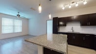 Located at 3603 Pavilion Palms Cir in Riverview, Florida, this single-floor residence offers a well-designed layout with modern finishes throughout. The open-concept kitchen and living area serve as the heart of the home, where rich espresso-toned cabinetry, a subway tile backsplash, and gleaming granite countertops create a polished, contemporary aesthetic. A large granite-topped island with pendant lighting provides both additional prep space and a natural gathering point. Stainless steel appliances, including a refrigerator, range, microwave, and dishwasher, complete the kitchen. Light wood-style flooring runs throughout the living and kitchen areas, complementing the neutral color palette and enhancing the sense of openness. The living room features a ceiling fan and large windows that invite natural light, with a sliding door providing access to the outdoors. The bedrooms are finished with plush carpeting, ceiling fans, and windows with blinds, offering a comfortable and restful atmosphere. Each bedroom includes closet storage. The bathrooms are thoughtfully appointed with large-format tile flooring, dark vanity cabinetry, granite countertops, and well-lit mirrors. The primary bathroom features a dual-sink vanity, while an additional bathroom includes a tub-shower combination with floor-to-ceiling tile surround.