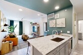 Located at 650 N Sgt Ed Holcomb Blvd in Conroe, TX, this thoughtfully designed one-bedroom, two-bathroom residence offers a modern living experience with refined finishes throughout. The open-concept kitchen and living area serves as the heart of the home, anchored by a striking granite-topped island with seating for three — ideal for casual dining or entertaining. The kitchen features gray shaker cabinetry, stainless steel appliances, recessed lighting, and a bold teal accent ceiling that adds a distinctive design element to the space. Light wood-tone flooring flows seamlessly through the main living areas, complemented by large windows dressed in dark curtains that allow for abundant natural light. The living area is bright and airy, with a ceiling fan overhead and access to a private balcony. The bedroom offers a comfortable retreat with plush carpeting, dual windows, a ceiling fan, and a direct connection to one of the two bathrooms. The bathrooms are finished with granite-topped gray vanities, tiled tub-shower combinations, and light wood flooring. Additional conveniences include three closets, an in-unit laundry area, and a hallway connecting the private spaces. A staircase provides access to the building's other levels.