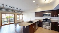 This well-appointed one-bedroom, one-bathroom unit at 468 Delaware Ave in Buffalo, NY offers a thoughtfully designed open-concept layout. The combined kitchen and living area serves as the heart of the space, featuring rich hardwood flooring, track lighting, and an exposed cylindrical duct that lends an industrial-modern character. The kitchen is outfitted with dark espresso cabinetry, granite countertops, a peninsula island with an undermount sink, and a full suite of stainless steel appliances including a gas range, microwave, and dishwasher. A stacked in-unit washer and dryer adds everyday convenience. Sliding glass doors open to a private balcony, flooding the living area with natural light and offering outdoor views of the surrounding neighborhood. A clean, well-lit hallway with hardwood floors connects the main living area to the private quarters. The bedroom features patterned carpet, a large wood-framed window, and access to both a closet and an additional storage area. The bathroom is finished with large-format dark tile flooring, a tiled walk-in shower, a dark-stained vanity with granite countertop, and modern fixtures throughout.