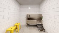 Located at 12 Leo M Birmingham Pkwy in Boston's Brighton neighborhood, this single-floor pet grooming room is purpose-built for pet care and maintenance. The space is defined by floor-to-ceiling white subway tile walls with clean gray grout lines, creating a bright, hygienic, and easy-to-maintain environment throughout.

The centerpiece of the room is a stainless steel dog wash tub, equipped with an integrated sprayer, a removable ramp for easy pet access, and a non-slip entry mat on wheels for added safety and convenience. A temperature-control dial is mounted directly into the tiled wall nearby, allowing precise water temperature adjustment. Yellow metal stools are positioned beside the tub, providing a practical seating option during grooming sessions.

A dedicated drying or grooming area is also present, featuring three bright yellow wall-mounted hooks for hanging tools, leashes, or accessories. Additional electrical outlets are conveniently placed at multiple points along the tiled walls. The concrete floor completes the utilitarian aesthetic, offering durability and easy cleanup. Overall, the space is thoughtfully designed to be functional, sanitary, and well-equipped for pet grooming needs.