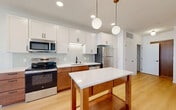 Located at 826 Williamson St in Madison, WI, this 2-bedroom, 1-bathroom unit offers a clean, modern aesthetic throughout its single-floor layout. Light hardwood flooring runs continuously across the space, complementing the bright white walls and creating a cohesive, contemporary feel.

The open-concept kitchen and living area serves as the heart of the unit. The kitchen is well-equipped with stainless steel appliances, including a refrigerator, range, microwave, and dishwasher. Two-tone cabinetry pairs warm wood lower cabinets with crisp white upper cabinets, accented by a subway tile backsplash and white quartz countertops. A freestanding island with a matching countertop provides additional workspace. Globe pendant lights with brass fixtures add a stylish touch overhead. The living area features large black-framed windows that invite abundant natural light.

The two bedrooms are bright and comfortably sized, each with large black-framed windows offering views of the surrounding neighborhood. The primary bedroom provides access to the shared bathroom, which features warm wood cabinetry, a white quartz vanity countertop, and black hardware accents. A built-in wall-mounted shelf near the entryway adds a practical organizational element to the space.