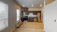 Located at 1408 21st Ave NW in Austin, Minnesota, this single-floor unit offers a thoughtfully designed layout with modern finishes throughout. Light wood-style flooring runs through the main living areas, complementing the clean, neutral color palette that gives the space a bright and welcoming feel.

The kitchen is a standout feature, outfitted with rich dark-stained cabinetry that extends to the ceiling for ample storage, granite countertops, and a full suite of stainless steel appliances including a range with over-the-range microwave, dishwasher, and refrigerator. A window allows natural light to fill the kitchen area.

The hallway connects the main living spaces efficiently, featuring a sliding barn door and recessed lighting overhead. An electrical panel is conveniently accessible along the corridor. The bedroom is carpeted for comfort and includes a spacious closet with a sliding panel door and built-in wire shelving, providing practical storage solutions.

The bathroom is well-appointed with the same dark cabinetry and granite vanity top seen in the kitchen, wood-style flooring, and a full tub/shower combination. The 3D layout view confirms a compact yet functional floor plan that makes excellent use of every square foot, making this unit a practical and stylish living option.