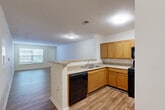 Located at Regents Center in Lexington, NC, this single-story residence offers a practical and comfortable layout across one bedroom, one bathroom, a combined kitchen and living area, a hallway, and a closet. The open-concept kitchen flows directly into the living room, creating a connected and functional common area. The kitchen is equipped with warm honey-toned cabinetry, ample upper and lower storage, light countertops, a peninsula with a sink, and a full suite of black appliances including a gas range, built-in microwave, dishwasher, and refrigerator. Wood-style plank flooring runs throughout the kitchen and living areas, adding warmth and easy maintenance. The living room is generously sized, bathed in natural light from a large window, and features the same durable flooring with a front entry door nearby. The bedroom offers a comfortable footprint with plush carpeting, a ceiling fan with light fixture, and a window that brings in natural light. The bathroom is outfitted with wood-style flooring, a full soaking tub and shower combination, and multiple stainless steel grab bars, reflecting an accessible and safety-conscious design. Textured ceilings are present throughout, completing the cohesive and functional character of this single-level residence.