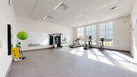Located at 3525 N Peoria Ave in Tulsa, Oklahoma, this fitness center offers a well-equipped, single-floor exercise space designed to support a full range of workout routines. The room features a clean, modern aesthetic with crisp white walls, a drop-panel ceiling with integrated linear lighting, and durable speckled flooring suited for high-traffic use.

Large, floor-to-ceiling multi-pane windows line one wall, flooding the space with generous natural light and providing open views of the surrounding exterior. A wall of mirrors runs along an adjacent wall, visually expanding the room and supporting form-checking during exercise.

The fitness center is equipped with a multi-function cable and weight machine, treadmills, an elliptical trainer, and a stationary bike, providing comprehensive cardio and strength training options. Additional accessories including a stability ball, medicine balls, resistance bands, and a pull-up bar station further enhance the variety of available workouts. Ample open floor space allows for stretching, mat exercises, or functional training. Multiple doors along the back wall provide convenient access and connectivity to adjacent areas. The bright, airy atmosphere and thoughtfully arranged equipment make this fitness center a practical and inviting space for daily exercise.