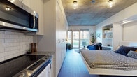 Located on Milwaukee's vibrant East Side, this contemporary studio at 1840 N Farwell Ave is thoughtfully designed to maximize functionality without sacrificing style. The open-plan layout features striking exposed concrete ceilings that lend an industrial character, complemented by warm hardwood-style flooring that runs throughout the space.

The fully equipped kitchen is outfitted with stainless steel appliances — including a refrigerator, electric range, dishwasher, and over-the-range microwave — along with granite countertops, a classic white subway tile backsplash, and crisp white cabinetry with open shelving for added storage and display.

The living area is anchored by large floor-to-ceiling sliding glass doors that flood the space with natural light and provide direct access to a private outdoor patio, offering views of the surrounding neighborhood. A built-in shelving and desk unit seamlessly integrates a workspace into the living area, while a wall of floor-to-ceiling white cabinetry delivers generous storage solutions.

The bathroom features a granite-topped vanity with white cabinetry, a large mirror, and wood-toned flooring, maintaining the clean, modern aesthetic found throughout. The overall ambiance is urban and contemporary, blending industrial design elements with refined, practical finishes ideal for city living.