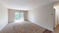 Located at 351 Andover Drive in Valparaiso, Indiana, this single-floor, one-bedroom, one-bathroom residence offers a straightforward and functional layout across five distinct spaces. The living room is a generously sized, carpet-floored area with neutral taupe walls and clean white trim. A sliding glass door floods the room with natural light and provides outdoor views of surrounding greenery, complemented by vertical blinds for privacy. The front entry opens directly into this welcoming space, where wood-look flooring transitions seamlessly from the entryway into the carpeted living area. The kitchen features warm beige cabinetry with ample upper and lower storage, dark laminate countertops, and a white coil-burner electric range with a built-in overhead ventilation hood. The bedroom is a well-proportioned, carpeted room with a window dressed in vertical blinds that invite natural light while maintaining a comfortable atmosphere. The bathroom is finished with white cabinetry, a drop-in sink with brushed nickel hardware, light tile flooring, and mirrored medicine cabinets above the vanity. A connecting hallway ties the rooms together, creating an efficient and easy-to-navigate floor plan throughout the home.