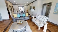 This single-floor space makes a strong first impression with its thoughtfully designed lounge area, blending comfort and contemporary style. The seating area is anchored by a plush gray leather sofa accented with vibrant teal and yellow throw pillows, complemented by a patterned accent chair in neutral tones that adds visual texture to the room. A round metallic coffee table serves as a refined centerpiece, topped with decorative orb accents that enhance the space's polished aesthetic.

Warm hardwood flooring runs throughout, grounding the space with a sense of inviting warmth, while a soft area rug beneath the seating arrangement adds comfort underfoot. Recessed lighting in the ceiling provides even illumination, and a statement table lamp with a bold geometric shade contributes an additional layer of ambient light and design interest.

Crown molding details and clean wall finishes lend the space a refined, professional character. Large glass entry doors at the far end allow generous natural light to flow in, creating a bright and open atmosphere. Decorative wall accents, including a sunburst mirror and ornamental pieces, add personality without overwhelming the space. Overall, the layout is open and functional, making it well-suited for welcoming guests or serving as a communal gathering area.