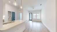 This well-designed 2-bedroom, 2-bathroom residence offers a thoughtful single-floor layout with contemporary finishes throughout. The open-concept kitchen and living area serves as the heart of the home, featuring light wood-look flooring, soaring ceilings, and large windows that invite generous natural light. The kitchen is outfitted with stainless steel appliances — including a side-by-side refrigerator, range, and microwave — paired with two-tone cabinetry, white subway tile backsplash, a built-in wine rack, and a spacious white quartz peninsula with pendant lighting overhead. A ceiling fan and direct outdoor access via a teal-accented door add function and character to the living area. The primary bedroom is generously sized, boasting its own en-suite bathroom complete with a dual-sink vanity featuring wood-toned cabinetry, a separate tiled shower with dark accent tile, and a walk-in closet. The second bedroom offers natural light through wide windows and light wood flooring. The second bathroom includes a full soaking tub and shower combo with elegant marble-look tile surround. Teal interior doors serve as a consistent, vibrant design accent throughout the space, complementing the clean, neutral palette and modern aesthetic.