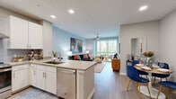 This 1-bedroom, 1-bathroom residence offers a thoughtfully designed open-concept layout that maximizes every square foot of its well-proportioned floor plan. Light wood-style flooring flows seamlessly throughout, anchoring the space with a clean, contemporary aesthetic.

The combined kitchen and living area serves as the heart of the home. The kitchen is equipped with stainless steel appliances — including a French door refrigerator, range with hood vent, and dishwasher — complemented by white cabinetry, a tile backsplash, and a quartz-topped peninsula with bar seating for three. The living room benefits from large sliding glass doors that open to a private balcony, flooding the space with natural light and providing views of surrounding greenery. A ceiling fan adds to the comfort of this airy, open gathering area.

The bedroom features a distinctive warm-toned accent wall, large windows with wooded views, a ceiling fan, and direct access to the bathroom. The bathroom presents a clean, elongated corridor with large-format tile flooring, a white vanity with ample storage, and a well-lit mirror.

A dedicated closet provides organized storage, while the in-unit laundry room houses a full-size washer and dryer with overhead shelving — a practical and convenient feature. Recessed lighting throughout maintains a bright, polished ambiance across the entire residence.
