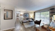 Located at 100 Ashley Creek Ct in Stone Mountain, Georgia, this two-bedroom, one-bathroom residence offers a well-designed single-floor layout with a cohesive blend of comfort and functionality. The living room serves as the heart of the home, showcasing rich wood-style flooring, a classic brick fireplace, and a large sliding glass door flanked by vertical blinds and plaid drapes that fill the space with natural light and provide access to an outdoor area. A hallway connects the main living spaces to the private quarters, creating a natural separation between common and personal areas. The dining room sits adjacent to the living area and features a pendant light fixture and a mirrored accent wall that enhances the sense of space. The kitchen offers dark cabinetry with sleek hardware, light countertops, a tile backsplash, and a pass-through opening to the dining room. The spacious primary bedroom includes dual closets and soft neutral tones, while the second bedroom offers plush carpeting and a bright window. The full bathroom features a tub-shower combination, a dark-cabineted vanity, and wood-style flooring consistent with the rest of the home. A dedicated laundry room with wire shelving and washer/dryer hookups adds everyday convenience to this well-appointed residence.