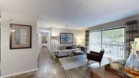 Located at 100 Ashley Creek Ct in Stone Mountain, Georgia, this two-bedroom, one-bathroom residence offers a well-designed single-floor layout with a cohesive blend of comfort and functionality. The living room serves as the heart of the home, showcasing rich wood-style flooring, a classic brick fireplace, and a large sliding glass door flanked by vertical blinds and plaid drapes that fill the space with natural light and provide access to an outdoor area. A hallway connects the main living spaces to the private quarters, creating a natural separation between common and personal areas. The dining room sits adjacent to the living area and features a pendant light fixture and a mirrored accent wall that enhances the sense of space. The kitchen offers dark cabinetry with sleek hardware, light countertops, a tile backsplash, and a pass-through opening to the dining room. The spacious primary bedroom includes dual closets and soft neutral tones, while the second bedroom offers plush carpeting and a bright window. The full bathroom features a tub-shower combination, a dark-cabineted vanity, and wood-style flooring consistent with the rest of the home. A dedicated laundry room with wire shelving and washer/dryer hookups adds everyday convenience to this well-appointed residence.