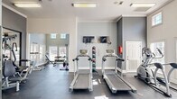 This fitness room in Columbia, SC offers a thoughtfully designed exercise space that accommodates a wide range of workout needs. The room features a striking blue tray ceiling accented by recessed lighting and two ceiling fans, which contribute to a comfortable and well-ventilated environment during workouts. White walls paired with the bold ceiling create a clean, modern aesthetic throughout.

The cardio section lines one wall with multiple treadmills, an elliptical, and a stationary bike, each positioned beneath wall-mounted flat-screen TVs for entertainment during exercise. Large windows and glass-paneled doors along the exterior wall allow ample natural light to fill the space and provide views of the outdoors, enhancing the overall workout atmosphere.

The strength training area includes a multi-station cable machine, a full rack of dumbbells, and various free weight benches, offering versatility for both beginners and experienced fitness enthusiasts. Floor-to-ceiling mirrors along one wall visually expand the space and allow users to monitor their form. The durable rubber flooring throughout provides both safety and comfort.

A built-in water fountain station is conveniently recessed into the wall, offering easy hydration access. The room's well-organized layout ensures ample space to move freely between equipment, making this fitness room a fully functional and inviting facility.