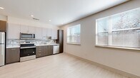 This thoughtfully designed studio presents a clean, modern aesthetic across a single level. The open-concept kitchen and living area forms the heart of the space, featuring light wood-look flooring that extends throughout, recessed lighting, and a ceiling fan that enhances airflow and comfort. Large windows fitted with blinds allow natural light to fill the room, creating a bright and airy atmosphere.

The kitchen is well-appointed with stainless steel appliances — including a refrigerator, electric range, over-the-range microwave, and dishwasher — complemented by two-tone cabinetry in white and dark wood finishes. White quartz countertops and a subway tile backsplash add a polished, contemporary touch, while ample upper and lower cabinet storage maximizes functionality.

The bathroom continues the modern design language with large-format gray tile flooring, a full soaking tub with white subway tile surround, a dark wood vanity with white countertop, and a framed mirror. Adjacent to the bathroom, the dedicated laundry area houses a stacked washer and dryer unit alongside built-in wire shelving for additional storage. The neutral color palette and consistent finishes throughout lend the space a cohesive, move-in-ready appeal.