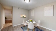 This two-story residence is designed with a clean, contemporary aesthetic characterized by neutral gray and white tones throughout. The main level opens into a comfortable living room featuring hardwood-style flooring, a large window that draws in natural light, and a carpeted staircase leading to the upper floor. Adjacent to the living area is a dedicated dining space, highlighted by a pass-through window connecting it directly to the kitchen, adding both functionality and an open feel.

The kitchen is equipped with white shaker-style cabinetry, granite-patterned countertops, stainless steel appliances including a range and dishwasher, and light hardwood-style flooring. A full bathroom on the main level features a tub-shower combination with light, neutral finishes.

Upstairs, two bedrooms offer carpeted flooring and windows providing natural light. Each room provides a quiet, restful atmosphere. A second bathroom on this level includes a walk-in shower, built-in shelving, and a white vanity, maintaining the home's consistent, minimal design language. Textured ceilings are present throughout, and the overall layout is efficiently organized across both levels.