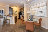 Located at 5801 Deauville Blvd in Midland, Texas, this single-floor residence offers a thoughtfully designed layout with an open-concept kitchen, a comfortable living room, multiple bedrooms, and two full bathrooms. The kitchen is outfitted with dark espresso cabinetry, granite countertops, stainless steel appliances including a range, microwave, and refrigerator, a light blue subway tile backsplash, and a peninsula island with bar seating — ideal for casual dining or entertaining. Wood-look flooring flows throughout the main living areas, complementing the warm, neutral wall tones. The living room features crown molding, a ceiling fan, a bold dark accent wall, and a glass door providing access to an outdoor area and natural light. The primary bedroom showcases a dramatic navy accent wall, ceiling fan, and plush carpeting, while a secondary bedroom benefits from a large window with outdoor views and ample natural light. Both bathrooms are finished with dark cabinetry, granite countertops, and wood-look flooring; the full bathroom includes a soaking tub and shower combination with tile surround. Throughout the residence, consistent design choices — including crown molding and a cohesive navy and neutral color palette — create a polished and cohesive living environment.