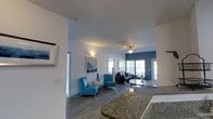 This single-floor, three-bedroom, three-bathroom residence combines functional design with modern style across a spacious and thoughtfully arranged floor plan. The open-concept living and dining area serves as the heart of the home, featuring durable wood-look flooring, a ceiling fan, and large windows that invite natural light and create a bright, welcoming atmosphere. A bold accent wall adds a contemporary touch to the living area, which is furnished with a comfortable sofa, a sleek glass coffee table, and coordinating blue accent chairs that lend the space a cohesive, stylish feel. The kitchen is well-equipped with black appliances, ample cabinetry, and a granite-topped counter with bar seating, flowing seamlessly into the dining area, which features a round table with seating for multiple guests. The primary bedroom is generously sized and accented with warm lighting and blue bedding, complementing the home's cool-toned color palette. Each of the three full bathrooms provides convenience and functionality. Throughout the home, clean white walls and consistent flooring create a unified aesthetic that feels both modern and livable. This residence is an excellent option for those seeking a spacious, move-in-ready home with a contemporary design sensibility.