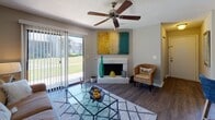 Located at Ashley Crossing Lane in Charleston, SC, this single-floor residence offers a thoughtfully designed layout with comfortable living spaces and functional features throughout. The living room serves as the heart of the home, highlighted by a brick fireplace, hardwood-style flooring, a ceiling fan, and a sliding glass door that fills the room with natural light and provides direct access to the outdoors. The adjacent galley-style kitchen is equipped with warm wood cabinetry, dark granite-style countertops, and a functional electric range, opening seamlessly into a dedicated dining area. The dining space accommodates a round table for four beneath a stylish pendant light and features a window with outdoor views. The primary bedroom is carpeted and generously sized, offering ample natural light through large windows and direct access to a walk-in closet with dual hanging rods. A second bedroom also features carpet flooring and a large window. Both bathrooms are well-appointed, each with a tub-shower combination, a vanity with wood cabinetry, granite-style countertops, and hardwood-style flooring. The overall ambiance is warm and inviting, with neutral tones and practical finishes carried consistently throughout the space.