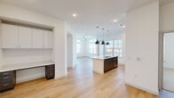 This well-designed 2-bedroom, 2-bathroom single-story home in Austin, TX offers a bright, modern living experience with a thoughtfully planned open-concept layout. The combined kitchen and living area serves as the heart of the home, featuring light hardwood-style flooring, recessed lighting, and large windows that flood the space with natural light. The kitchen is appointed with two-tone dark lower and white upper cabinetry, a subway tile backsplash, stainless steel appliances, and a central island with a white quartz countertop and pendant lighting overhead. A convenient built-in desk area adds functional versatility to the space. The primary bedroom is generously sized, showcasing oversized windows with transom panes that frame outdoor views and fill the room with daylight. It includes a spacious walk-in closet with dual hanging rods and shelving. The second bedroom features plush carpeting, a ceiling fan, and its own closet. Both bathrooms are finished with dark tile flooring, dark cabinetry, and clean white countertops. A connecting hallway with a tray ceiling detail links the living areas to the private quarters. Throughout, the home maintains a clean, contemporary aesthetic with crisp white walls and consistent finishes.