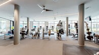 Located at 770 N Eldridge Pkwy in Houston, TX, this fitness center spans a single floor and is divided into two distinct exercise rooms, offering a comprehensive workout environment for a wide range of fitness needs.

The main exercise room is a generously sized, open-concept space defined by floor-to-ceiling windows that line the perimeter, flooding the area with natural light and providing views of the surrounding outdoor courtyard. Cylindrical columns punctuate the layout, while ceiling fans and linear LED lighting contribute to a clean, modern aesthetic. The room is outfitted with a robust selection of cardio equipment — including treadmills, ellipticals, and stationary bikes — alongside a variety of strength-training machines, free weights, and stability balls, all arranged on protective rubber mats over neutral-toned carpet. A wall-mounted television and informational signage add functional touches near the entry area.

The second exercise room serves as a dedicated cycling and functional training studio, featuring hardwood flooring, a row of spin bikes positioned along the window wall, and full-length mirrors that enhance the sense of space. This room benefits from direct outdoor access through glass-paneled doors, adding to the bright, airy atmosphere. Together, the two rooms provide a well-rounded, thoughtfully designed fitness facility.