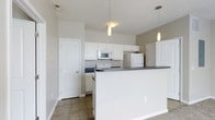 Located at 8181 Herald Cv in Blacklick, Ohio, this single-floor residence offers a practical and well-appointed layout designed for comfortable everyday living. The kitchen serves as a central highlight of the home, showcasing crisp white cabinetry that extends to the upper walls, providing generous storage throughout. Dark countertops offer a clean contrast against the white finishes, while a peninsula-style breakfast bar creates a natural division between the kitchen and the adjoining living area, adding both functionality and casual dining space. White appliances, including a range, microwave, and refrigerator, are neatly integrated into the cabinetry for a cohesive look. Pendant lighting hangs above the kitchen area, casting warm, focused light that enhances the overall ambiance. The tile flooring in the kitchen transitions seamlessly into the surrounding spaces, contributing to the home's clean and consistent aesthetic. The neutral wall tones throughout create a bright, open feel, making the interior feel welcoming and easy to personalize. A convenient interior door off the kitchen provides access to additional storage or utility space. Overall, this home presents a straightforward, move-in-ready layout well-suited for those seeking a low-maintenance, single-level living experience in the Blacklick community.