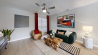 This thoughtfully designed single-floor residence offers two bedrooms, two bathrooms, and a functional layout that maximizes every square foot. The living room is a welcoming gathering space featuring light wood-look flooring, a textured ceiling, and a ceiling fan, with large windows dressed in bold red curtains that invite natural light. The open flow connects seamlessly to the dining area, which benefits from a sliding glass door overlooking a private outdoor space, creating a bright and airy atmosphere. The kitchen is well-equipped with gray cabinetry, a white subway tile backsplash, stainless steel appliances, and a built-in open pantry for added storage convenience. Both bathrooms are finished with striking marble-look tile surrounds in the tub/shower combinations, complemented by wood-look flooring and gray vanities. The primary bedroom is a comfortable retreat with a ceiling fan, soft carpeting, and ample natural light, while the second bedroom mirrors the same cozy, well-finished aesthetic. A dedicated hallway connects the private quarters to the main living spaces, and two closets provide practical storage throughout. The consistent use of neutral gray tones, modern fixtures, and light flooring gives the entire residence a cohesive, contemporary feel.