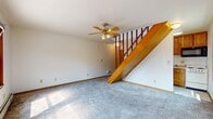Located at 428 S Walnut Ave in Ames, Iowa, this two-story unit offers 610 square feet of living space spread across two floors — 290 square feet on the lower level and 330 square feet on the upper level. The interior is finished with wall-to-wall carpeting throughout and features neutral white walls, creating a clean and functional aesthetic.

The lower level includes a living area with a wood-trimmed staircase, ceiling fan with light fixture, and baseboard heating — a practical heating solution seen consistently throughout the unit. Natural light enters generously through wood-framed windows, which offer views of the surrounding neighborhood.

The upper floor houses a spacious bedroom with dual windows, a ceiling fan, and a window-mounted air conditioning unit, complemented by baseboard heating. A full bathroom on this level includes a single-sink vanity with oak cabinetry, a toilet, and a tub-shower combination with sliding frosted glass doors and tile flooring. A carpeted walk-in closet provides ample storage with multiple wire shelving racks along the walls.

The unit's open upper landing, enclosed by a decorative wrought iron and wood railing, adds a distinctive architectural touch. Overall, the space is straightforward and functional, suited for individual or small-household occupancy in a residential Ames neighborhood.