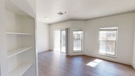 This single-floor unit offers a clean, modern interior designed with both comfort and functionality in mind. The living area is spacious and filled with natural light, courtesy of multiple windows and a sliding glass door that opens to an outdoor space. Wood-style flooring runs throughout, complementing the crisp white walls and adding warmth to the open layout. Built-in shelving near the living area provides convenient storage and display options.

The kitchen is well-appointed with white shaker-style cabinetry, granite countertops with a subtle speckled pattern, a classic subway tile backsplash, and stainless steel appliances including a dishwasher, range, and over-the-range microwave. A stainless steel sink completes the efficient workspace.

The bedroom features the same wood-style flooring, a ceiling fan with light fixture, and a window that allows natural light to filter in, creating a comfortable and airy atmosphere.

The bathroom is finished with granite countertops matching the kitchen, gray cabinetry with brushed nickel hardware, a large mirror, and a full tub-shower combination with a curved curtain rod. The consistent finishes throughout the unit give the space a cohesive, polished feel overall.