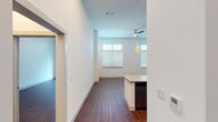 This well-appointed single-floor residence offers a thoughtfully designed open layout enhanced by notably high ceilings and rich, dark hardwood-style flooring that flows consistently throughout. The kitchen serves as a central focal point, showcasing dark espresso cabinetry, a white subway tile backsplash, stainless steel appliances including a refrigerator and microwave, and a generous granite-topped island with an integrated sink. Stylish pendant lights hang above the island, complementing the recessed ceiling fixtures. The kitchen opens directly into a bright living area bathed in natural light from multiple large windows fitted with horizontal blinds. A ceiling fan adds both comfort and character to the living space. The bedroom is generously proportioned with towering ceilings, and benefits from direct access to both a full bathroom and a walk-in closet. The bathroom features a tiled tub-shower combination with a curved curtain rod, granite vanity countertop, and dark cabinetry consistent with the overall design palette. A dedicated laundry room provides added convenience, complete with washer and dryer connections, a granite-topped cabinet, wire shelving, and hardwood-style flooring. The cohesive, contemporary aesthetic throughout makes this a functional and visually refined living space.