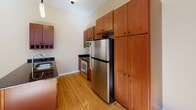 Located at 360 Robert St N in Saint Paul, Minnesota, this single-floor unit blends urban character with functional design. Warm hardwood flooring extends throughout the main living areas and bedrooms, lending a cohesive, inviting feel to the space.

The open living area is bathed in natural light through multiple large windows fitted with blinds, offering views of the surrounding cityscape. A structural column adds an architectural element to the space without compromising its openness.

The kitchen is well-appointed with rich wood cabinetry reaching toward the ceiling, dark granite countertops, stainless steel appliances including a refrigerator, microwave, and range, and a peninsula that provides both additional prep space and a natural division between the kitchen and living areas. A track lighting fixture overhead adds a contemporary touch.

The bedroom features hardwood floors, multiple windows, and a stylish sliding barn door that opens to a walk-in closet equipped with wire shelving and hanging rods, offering generous storage.

The bathroom is finished with a dark granite vanity, warm wood cabinetry, a tub-shower combination, and marble-style tile flooring, creating a clean and practical space. Overall, the unit offers a comfortable urban living environment with thoughtful finishes throughout.