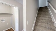 Located at 3818 S Rock Quarry Rd in Columbia, Missouri, this two-story, three-bedroom, three-bathroom home offers a functional and comfortable layout across two floors. The main level features a combined kitchen and living area, where the galley-style kitchen stands out with warm oak cabinetry, white countertops, recessed lighting, black appliances, and a window that brings in natural light. The living room is finished with hardwood-style flooring and opens directly to a wood deck through sliding glass doors, offering pleasant outdoor views and excellent indoor-outdoor flow. A dedicated laundry area with washer and dryer hookups and built-in shelving adds convenience on this floor. The bathrooms are clean and well-appointed, featuring tub-shower combinations, updated grey vanities, and hardwood-style flooring. The bedrooms are spread across both levels, with the generously sized primary bedroom offering a ceiling fan, carpet flooring, and a bright window. Additional bedrooms each include built-in closets with bi-fold doors and soft carpet underfoot. A hallway and staircase connect the two floors seamlessly. Neutral warm-beige tones throughout create a cohesive, move-in-ready ambiance suited for comfortable everyday living.