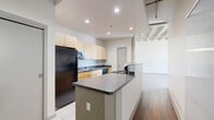 Located at 2010 Euclid Ave in Cleveland, Ohio, this three-bedroom, two-bathroom loft-style residence showcases a distinctive industrial aesthetic rooted in its architectural character. The single-floor layout offers a well-organized arrangement of rooms, including a combined dining and living area, three bedrooms, two bathrooms, three closets, a dedicated laundry space, and a balcony.

The open living and dining area is defined by exposed wooden beam ceilings, painted brick accent walls, and rich hardwood flooring that together create a warm yet industrial atmosphere. Large windows and a glass balcony door flood the space with natural light while providing views of the Cleveland skyline. The kitchen features light maple cabinetry, dark countertops, a central island, and tile flooring, with black appliances including a refrigerator, dishwasher, and microwave.

The bedrooms are carpeted for comfort, with exposed ductwork and brick detailing carrying the industrial theme throughout. One bathroom includes a full tub-shower combination with clean white surrounds, while the second features a wood-toned vanity with tile flooring. The balcony offers additional outdoor space with urban views, completing this characterful urban residence.