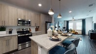 Located at 2429 Americana Blvd in Orlando, FL, this single-floor residence offers a thoughtfully designed open-concept layout that seamlessly connects the kitchen, dining, and living areas. The kitchen is a standout feature, showcasing light wood cabinetry, granite countertops, a full suite of stainless steel appliances, a tile backsplash, and a central island with pendant lighting — ideal for both cooking and casual dining. Dark hardwood-style flooring flows throughout the main living areas, creating a warm contrast to the neutral walls and modern finishes. The living room is bright and welcoming, benefiting from natural light through large windows with blinds and drapery, a ceiling fan, and ample wall space accented by bold, colorful artwork. The bedroom continues the contemporary aesthetic with plush carpeting, a teal accent wall, large windows, and generous natural light. The bathroom features a wood-toned vanity with granite countertops, an undermount sink, a large framed mirror, and a tiled walk-in shower, all complemented by dark hardwood-style flooring. Throughout the space, a cohesive blue, gold, and neutral color palette ties each room together, creating a modern and inviting atmosphere.