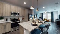 Located at 2429 Americana Blvd in Orlando, FL, this single-floor residence offers a thoughtfully designed open-concept layout that seamlessly connects the kitchen, dining, and living areas. The kitchen is a standout feature, showcasing light wood cabinetry, granite countertops, a full suite of stainless steel appliances, a tile backsplash, and a central island with pendant lighting — ideal for both cooking and casual dining. Dark hardwood-style flooring flows throughout the main living areas, creating a warm contrast to the neutral walls and modern finishes. The living room is bright and welcoming, benefiting from natural light through large windows with blinds and drapery, a ceiling fan, and ample wall space accented by bold, colorful artwork. The bedroom continues the contemporary aesthetic with plush carpeting, a teal accent wall, large windows, and generous natural light. The bathroom features a wood-toned vanity with granite countertops, an undermount sink, a large framed mirror, and a tiled walk-in shower, all complemented by dark hardwood-style flooring. Throughout the space, a cohesive blue, gold, and neutral color palette ties each room together, creating a modern and inviting atmosphere.