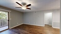 Located at 617 Richardson St in Simpsonville, South Carolina, this single-story, one-bedroom, one-bathroom residence offers a practical and comfortable layout across a compact but well-organized floor plan. Rich, dark hardwood-style flooring runs throughout the main living areas and bedroom, providing a warm and cohesive aesthetic complemented by neutral gray walls and white trim.

The living room is bright and inviting, featuring a ceiling fan with light fixture and a sliding glass door that opens to a private balcony, allowing natural light to pour in while offering pleasant views of the surrounding greenery. The bedroom is a comfortable size, fitted with its own ceiling fan and a window with blinds for natural light and privacy.

The galley-style kitchen is efficiently designed with warm wood cabinetry lining both sides, light countertops, a stainless steel sink, and white appliances including a refrigerator and range. A doorway from the kitchen connects to a dedicated laundry area with tile flooring. The bathroom includes a full tub-shower combination with clean white surround walls. Additional spaces include a hallway and closet, rounding out a functional and efficient single-floor layout ideal for comfortable everyday living.
