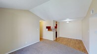 This single-floor space in Sherman offers an open, airy layout defined by striking vaulted ceilings that add a sense of height and spaciousness to the main living area. The living room is finished with soft, neutral-toned carpet that creates a comfortable, welcoming atmosphere, while the clean, light-colored walls throughout contribute to a bright and understated aesthetic.

A half-wall partition separates the living area from the kitchen, maintaining visual connectivity between the two spaces while providing a natural sense of division. The kitchen features rich, warm-toned wood cabinetry paired with hardwood-style flooring, offering a contrast to the carpeted living space. Appliances including a microwave are built into the cabinetry, contributing to a functional and cohesive design.

The transition between the living and kitchen areas flows naturally, with the open floor plan creating a versatile environment suited to both everyday living and entertaining. The textured ceiling in portions of the space adds subtle dimension, and the overall neutral palette provides a flexible backdrop adaptable to various interior styles. The single-floor layout ensures ease of navigation throughout.