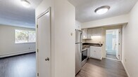 This efficient 2-bedroom, 1-bathroom unit is thoughtfully laid out across a single floor, making practical use of every square foot. The kitchen is a standout feature, equipped with stainless steel appliances including a smooth-top range, built-in microwave, dishwasher, and refrigerator. White cabinetry with dark granite-style countertops provides ample storage and prep space, while wood-look vinyl plank flooring adds a clean, modern touch.

The primary bedroom is generously sized relative to the overall footprint and features plush carpeting, a double sliding closet, and an additional secondary closet for extra storage. The second bedroom, also finished with wood-look flooring, offers a bright and versatile space suitable for sleeping, a home office, or other uses.

Natural light filters into the living area and bedrooms through lattice-style windows, with views of surrounding greenery. Baseboard heating is present throughout, ensuring comfort year-round. The bathroom is clean and functional, featuring a full tub-shower combo with light blue surround, a white vanity, and a large mirror.

The overall aesthetic is neutral and move-in ready, with light-toned walls throughout creating a bright, welcoming atmosphere in every room.