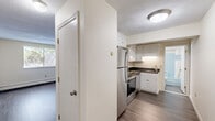 This efficient 2-bedroom, 1-bathroom unit is thoughtfully laid out across a single floor, making practical use of every square foot. The kitchen is a standout feature, equipped with stainless steel appliances including a smooth-top range, built-in microwave, dishwasher, and refrigerator. White cabinetry with dark granite-style countertops provides ample storage and prep space, while wood-look vinyl plank flooring adds a clean, modern touch.

The primary bedroom is generously sized relative to the overall footprint and features plush carpeting, a double sliding closet, and an additional secondary closet for extra storage. The second bedroom, also finished with wood-look flooring, offers a bright and versatile space suitable for sleeping, a home office, or other uses.

Natural light filters into the living area and bedrooms through lattice-style windows, with views of surrounding greenery. Baseboard heating is present throughout, ensuring comfort year-round. The bathroom is clean and functional, featuring a full tub-shower combo with light blue surround, a white vanity, and a large mirror.

The overall aesthetic is neutral and move-in ready, with light-toned walls throughout creating a bright, welcoming atmosphere in every room.