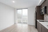 This single-floor unit showcases a cohesive modern design throughout its thoughtfully arranged spaces. The kitchen is a standout feature, outfitted with rich dark wood cabinetry extending floor to ceiling, stainless steel appliances including a full-size refrigerator and built-in microwave, light quartz countertops, and an eye-catching mosaic tile backsplash in a pattern of red, black, white, and grey — a detail that adds artistic character to the space.

The living area is bright and open, benefiting from a floor-to-ceiling glass sliding door that frames urban views and draws in generous natural light. Light-toned hardwood-style flooring runs throughout the main living spaces, contributing to the unit's clean, contemporary aesthetic.

The bathroom continues the mosaic tile motif, featuring a full soaking tub and shower combination enclosed by large-format white subway tiles. A striking vertical mosaic tile accent strip — mirroring the kitchen backsplash design — serves as a bold focal point. Dark slate-style floor tiles ground the bathroom space with contrast and texture.

A small utility panel is conveniently recessed into the hallway wall, and the overall layout, as revealed by the 3D scan, flows efficiently from the entry through the main living and kitchen areas toward the bathroom.