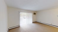 This single-floor unit is thoughtfully laid out across several distinct spaces, each designed with functionality in mind. The living area serves as the central gathering space, highlighted by a large sliding glass door dressed with vertical blinds that allows natural light to flood the room and provides outdoor access. A wall-mounted air conditioning unit and baseboard heating ensure year-round comfort throughout the space.

Adjacent to the living area, a dining space with ceiling fan lighting connects seamlessly to the kitchen. The kitchen features warm wood cabinetry, white laminate countertops, a stainless steel sink, and includes a dishwasher, refrigerator, and electric range. Light hardwood-style flooring completes the practical workspace.

The bedroom is carpeted and well-lit, equipped with a ceiling fan and a window that invites natural light. Baseboard heating runs along the perimeter, consistent with the rest of the unit.

The bathroom is finished with distinctive blue mosaic wall tiles extending halfway up the walls, complemented by light tile flooring, a vanity with mirror, and clean white fixtures. Overall, the unit presents a straightforward, functional design with neutral tones throughout.