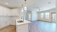 This well-appointed 2-bedroom, 2-bathroom residence offers a thoughtfully designed single-floor layout that balances modern aesthetics with functional living. The open-concept kitchen and living area serves as the heart of the home, where the kitchen stands out with crisp white shaker cabinetry adorned with brushed gold hardware, a classic white subway tile backsplash, quartz countertops, stainless steel appliances, and a peninsula island with a double sink illuminated by elegant pendant lighting. The living area flows seamlessly from the kitchen, featuring light-toned luxury vinyl plank flooring, a ceiling fan, and large windows alongside a glass-panel door that opens to a private balcony overlooking the exterior. Both bedrooms are carpeted and feature ceiling fans and natural light from well-sized windows. The spacious primary bedroom includes a walk-in closet outfitted with multi-tier wire shelving and hanging rods. The bathrooms are finished in a clean, contemporary style, with white cabinetry featuring gold hardware, wood-look flooring, and a tiled tub-shower combination with brushed nickel fixtures. Two dedicated closets provide ample storage throughout. The overall ambiance is bright, clean, and move-in ready.
