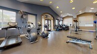 Located at 5095 Haven Pl in Dublin, CA, this fitness center offers a comprehensive workout facility designed to accommodate a wide range of exercise needs. The space is defined by its striking vaulted ceilings, which lend an open, airy quality throughout, while recessed lighting and large windows with slatted blinds ensure the interior is bright and welcoming.

The facility is divided into distinct workout zones. The cardio area is generously appointed with multiple elliptical trainers, stationary bikes, treadmills, and a rowing machine, all arranged to allow comfortable spacing between users. The strength training section features a multi-station cable machine, a dedicated weight bench, a rack of kettlebells and dumbbells, and additional resistance equipment, providing options for both machine-based and free weight training. Stability balls and accessories are also available for functional fitness exercises.

A full-length mirror in the strength zone enhances the sense of space while allowing users to monitor form. The flooring throughout is a durable, rubberized surface suited for high-traffic fitness use. An arched entryway with glass-paned double doors serves as an elegant architectural focal point, adding a refined touch to the functional environment. Industrial wall-mounted fans contribute to airflow and comfort. The overall ambiance is clean, organized, and purpose-built for an effective fitness experience.