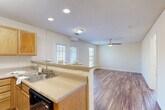 Located at 5034 Hilltop Rd in Greensboro, NC, this well-appointed one-bedroom, one-bathroom residence offers a practical and comfortable single-floor layout. The open-concept kitchen and living area forms the heart of the home, where warm-toned hardwood-style flooring flows seamlessly throughout. The kitchen is fully equipped with light oak cabinetry, black appliances including a refrigerator, electric range, microwave, and dishwasher, paired with ample counter space and a double sink. A peninsula with an overhanging breakfast bar connects the kitchen to the living area, which is brightened by multiple windows with slatted blinds and finished with a ceiling fan for year-round comfort. Recessed and track lighting add a clean, modern touch overhead, complemented by textured ceilings throughout. The bedroom offers a cozy carpeted floor, a ceiling fan with light, and direct access to a generously sized walk-in closet outfitted with wire shelving on multiple walls. The bathroom features warm hardwood-style flooring, an oak vanity with a large mirror, and a shower-tub combination. A dedicated utility room and additional closet space round out this efficiently designed residence.