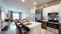 This well-appointed single-floor residence offers a thoughtfully designed open-concept layout that seamlessly connects the kitchen, dining, and living areas. The kitchen is a standout feature, boasting two-tone cabinetry in charcoal gray and crisp white, stainless steel appliances including a French door refrigerator, electric range, and microwave, complemented by a gray tile backsplash and light quartz countertops. A spacious island with bar seating provides both additional prep space and a casual dining option. The living room is bright and inviting, with a ceiling fan, large windows that bring in natural light and outdoor views, and a built-in window bench. Wood-look flooring flows throughout the common areas, adding warmth and continuity. The primary bedroom is generously sized, featuring a large window and access to a walk-in closet with ample built-in shelving and hanging rods. The primary bathroom offers a dual-sink vanity with dark cabinetry and quartz counters, plus a tub-shower combination with subway tile surround. A second bedroom is similarly well-lit, and its adjoining bathroom features a glass-enclosed walk-in shower with white tile and a single-sink vanity, maintaining the same refined design palette found throughout the space.