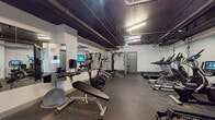 This fitness center in Memphis, TN offers a comprehensive workout environment within a single, efficiently utilized space. The room features an exposed dark ceiling with visible ductwork and pipe infrastructure, lending it an industrial aesthetic, while bright linear lighting ensures the area is well-illuminated throughout.

The cardio zone is lined with Spirit-brand treadmills, elliptical trainers equipped with interactive touchscreen displays, and a recumbent bike, providing a strong selection of aerobic equipment. A dedicated strength training area features a multi-functional cable machine, a Hoist adjustable weight bench, and a Peloton-style stationary bike with a digital monitor. Full-length wall mirrors expand the visual depth of the space and allow users to monitor their form during exercise.

The free weights section includes a structured dumbbell rack with a range of weights, complemented by additional benches for targeted lifting exercises. A functional training corner houses stability balls in multiple sizes, an Echelon rowing machine, and various accessory equipment ideal for dynamic and flexibility-focused workouts. Durable rubber flooring covers the entire space, providing safety and support underfoot. The overall layout is practical and thoughtfully arranged to accommodate a wide range of fitness routines within a compact footprint.