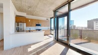 Located at 1717 South Michigan Avenue in Chicago's South Loop, this modern 2-bedroom, 2-bathroom unit offers a thoughtfully designed open-concept layout with contemporary finishes throughout. The combined living, dining, and kitchen area serves as the heart of the home, featuring striking exposed concrete ceilings, wide-plank wood-tone flooring, and floor-to-ceiling windows that flood the space with natural light and frame sweeping city views. A large sliding glass door opens directly onto a private balcony, seamlessly connecting indoor and outdoor living. The kitchen is outfitted with warm wood cabinetry, white subway tile backsplash, stainless steel appliances including a gas range, and a spacious white waterfall island ideal for dining and entertaining. The primary bedroom is generously sized, offering large windows with urban views, an exposed concrete ceiling, and access to a walk-in closet with built-in wire shelving. The second bedroom provides a bright and flexible space with light wood flooring. Both bathrooms are finished with wood-toned vanities, light tile flooring, and matte black fixtures. Additional features include four closets, a dedicated laundry area, and a hallway with sleek sliding panel doors, completing this well-appointed urban residence.