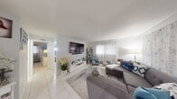 Located at 1908 Northwest 4th Avenue in Boca Raton, FL, this single-story, 3-bedroom, 2-bathroom home offers a well-organized and functional layout. The living room serves as the heart of the home, featuring light-toned tile flooring, a large wall-mounted television, and a generous sectional sofa. Sheer floral curtains allow natural light to filter in, creating a warm and inviting atmosphere.

The kitchen is a standout feature, equipped with stainless steel appliances including a range, microwave, and refrigerator. Gray shaker-style cabinetry pairs with a mosaic tile backsplash and a skylight detail in the ceiling, lending the space both style and brightness. Recessed lighting further enhances the clean, modern aesthetic.

The spacious primary bedroom includes a wall-mounted television, a large multi-drawer white dresser, and access to a walk-in closet area. A second bedroom accommodates twin beds with ample space between them. Both bathrooms feature tile surrounds, tub-shower combinations, and white vanities with marble-style countertops — one highlighted by a backlit round mirror.

Throughout the home, consistent tile flooring and a neutral white-and-gray color palette create a cohesive and airy feel well-suited to the sunny South Florida climate.