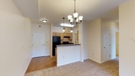 This single-floor residence offers a practical and comfortable layout designed for everyday living. The open-concept living and dining area is anchored by elegant chandelier lighting and transitions seamlessly between plush carpeted flooring and hardwood-style flooring near the entryway. A breakfast bar separates the living space from the kitchen, which features a galley-style design with light wood cabinetry, dark countertops, and black appliances including an electric range and dishwasher. The kitchen also provides direct access to a utility area housing the electrical panel.

The bedrooms are carpeted and filled with natural light from windows fitted with blinds, offering a quiet and versatile space. Two full bathrooms serve the residence: one includes a shower-tub combination with a wide vanity mirror and wood cabinetry, while the second features a walk-in shower and a similarly styled vanity. Both bathrooms are finished with tile flooring and warm, neutral tones. A dedicated laundry closet is equipped with washer and dryer hookups and an overhead wire shelving rack, adding to the unit's convenience. Throughout the space, neutral wall colors and clean white trim create a bright, move-in-ready atmosphere.